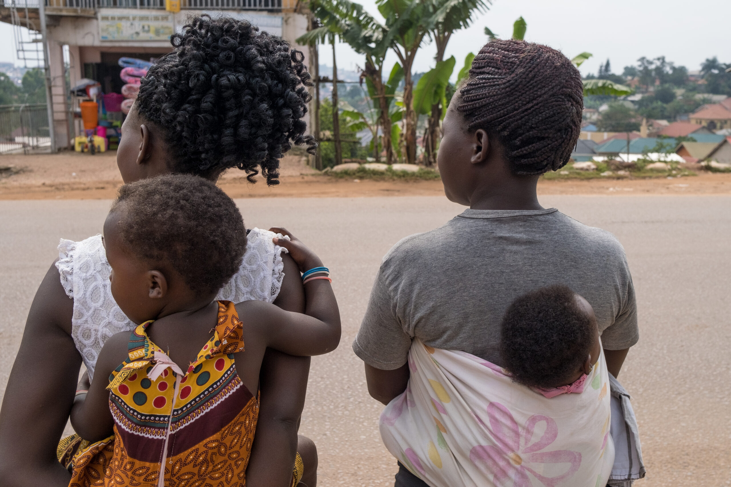 Mary Nabukenya, 25, (L) waits to cross the road with her children after work, accompanied by her friend Joan (R) in Kampala, Uganda, on February 18, 2021. Since COVID-19, schools in Uganda have been closed to most age years, and children spend their time at home.